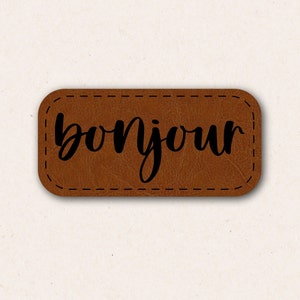 May include: A brown leather patch with the word "bonjour" written in black cursive lettering.