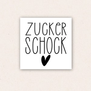 May include: White card with black text that reads "Zucker Schock" with a black heart below the text.