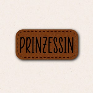 Może przedstawiać: Brązowa skórzana etykieta z obszytym brzegiem i napisem "PRINZESSIN" czarnymi literami.