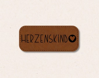 May include: Brown leather label with the text "HERZENSKIND" and a small heart symbol.