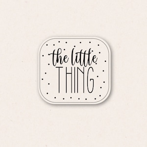 May include: A white square sticker with a black dotted border and the text "the little thing" in black cursive lettering.