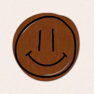 Op de afbeelding: Een bruin leren patch met een zwart smiley-gezicht erop getekend.