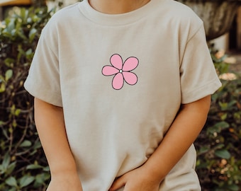 May include: A light beige t-shirt with a pink flower graphic on the front.