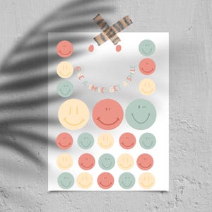Puede incluir: Un póster blanco con una colección de pegatinas de caras sonrientes de colores en varios tamaños y colores, incluyendo melocotón, amarillo y verde. El texto "GIVE A SMILE GET A SMILE" está escrito en semicírculo. El póster está pegado a una pared con cinta adhesiva decorativa.