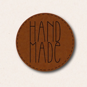 May include: A brown leather circle tag with a stitched border and the text "HAND MADE" in black.