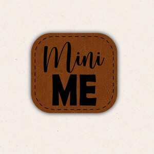 May include: A brown leather patch with the text "Mini Me" in black lettering.