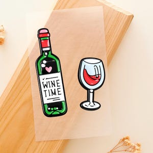 Puede incluir: Ilustración colorida de una botella de vino verde con un corazón rosa y la inscripción "WINE TIME" en una etiqueta blanca. Al lado, una copa de vino llena de vino tinto. La imagen está sobre un papel translúcido.