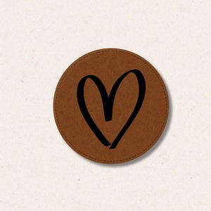 Könnte beinhalten: Ein brauner Lederuntersetzer mit einem schwarzen Herzdesign.