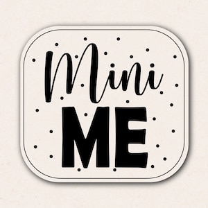 May include: A white square sign with black polka dots and the text "Mini Me" in black.