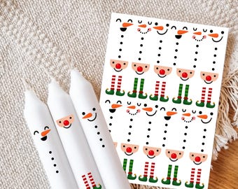 May include: Three white taper candles decorated with snowman and elf graphics, accompanied by a rectangular sheet of matching stickers featuring repeating patterns of snowman faces, red noses, and striped elf legs in red and green colors.
