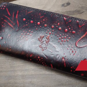 May include: A black leather wallet with a red and black pattern. The wallet has a zipper closure and a deer head logo. The text "PDF" is visible in the lower right corner of the image.