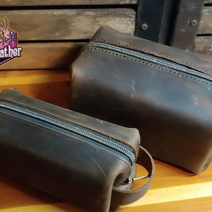 May include: Two brown leather zippered pouches with a VrnC Leather logo. The larger pouch has a strap handle.
