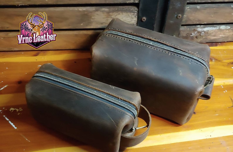May include: Two brown leather zippered pouches with a VrnC Leather logo. The larger pouch has a strap handle.
