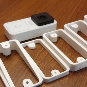 May include: A set of seven white plastic 3D printed wall mounts for a doorbell camera. The mounts are designed to fit a variety of doorbell cameras and are easy to install.