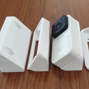 May include: Five white plastic pieces for mounting a doorbell camera. The pieces include two corner brackets, two wall plates, and the doorbell camera itself.