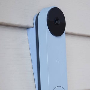 May include: A light blue doorbell camera with a black lens and a white button. The camera is mounted on a white wall.