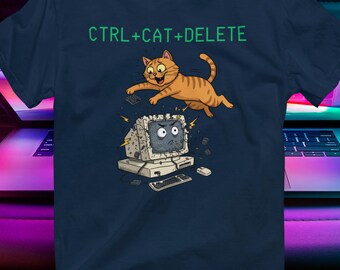 Op de afbeelding: Marineblauw t-shirt met de tekst "CTRL+CAT+DELETE" boven een cartoon illustratie van een oranje kat die over een kapotte computer springt. Het ontwerp is gedrukt op een donkerblauwe tee.