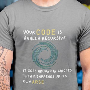 Peut inclure: Un t-shirt gris avec le texte "YOUR CODE IS ANALLY RECURSIVE" en blanc et jaune. En dessous, un motif en spirale bleu et vert. Le texte "IT GOES AROUND IN CIRCLES THEN DISAPPEARS UP ITS OWN ARSE" est en dessous. Le t-shirt est porté par une personne.