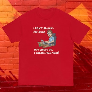 Op de afbeelding: Rood t-shirt met de tekst "I DON'T ALWAYS FIX BUGS BUT WHEN I DO, I CREATE FIVE MORE!" en een cartoon van een persoon die op een laptop werkt. De persoon draagt een bril en een blauw shirt.