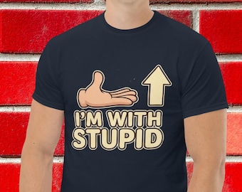 Könnte beinhalten: Marineblaues T-Shirt mit dem cremefarbenen Text "I'M WITH STUPID", einer Cartoon-Hand und einem Pfeil nach oben. Das T-Shirt hat einen Rundhalsausschnitt.