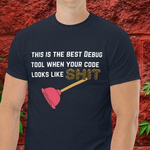 Peut inclure: T-shirt bleu marine avec le texte blanc "THIS IS THE BEST DEBUG TOOL WHEN YOUR CODE LOOKS LIKE SHIT". Un déboucheur rose avec un manche en bois est présent. Un article humoristique pour les programmeurs.