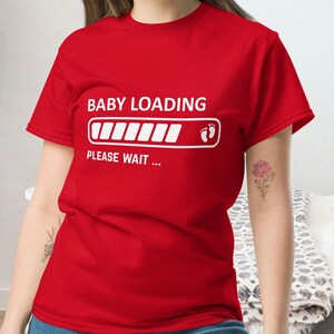 May include: Red t-shirt with the text "BABY LOADING" above a progress bar graphic, and "PLEASE WAIT ..." below. The progress bar shows the baby is almost ready. A fun and cute pregnancy announcement tee.
