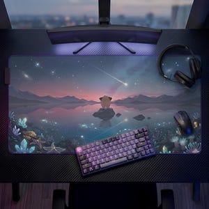 May include: A large rectangular desk mat featuring a printed illustration of a starry night sky over a calm lake with mountains, a small creature on a rock, and glowing underwater crystals. A black mechanical keyboard and mouse sit on the mat.