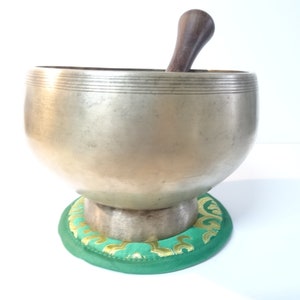 Pode incluir: Uma tigela de canto prateada com um batedor de madeira, descansando sobre um almofada verde e dourada.