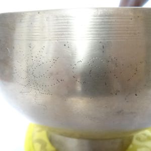 Pode incluir: Uma tigela de canto prateada com um padrão decorativo de pontos. A tigela está sentada em uma almofada amarela.