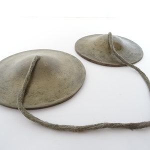 May include: Two small, round, gray metal cymbals with a rope connecting them.