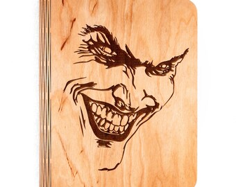 Puede incluir: Una caja de madera con una imagen grabada con láser de la cara del Joker, con una amplia sonrisa de dientes.