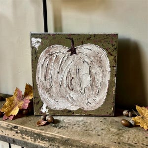 May include: A square canvas painting featuring a textured, off-white pumpkin with a dark brown stem centered on a distressed olive green background. The pumpkin surface displays a cracked, layered paint effect with visible brushstrokes and depth.