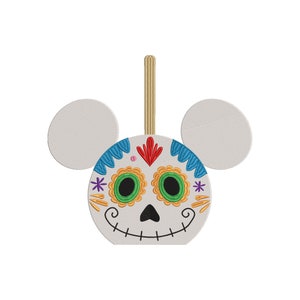 May include: A white and blue sugar skull ornament with Mickey Mouse ears. The skull has a colorful Day of the Dead design with green eyes, a red nose, and yellow flowers.