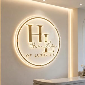 May include: A circular wall sign featuring a gold-toned metallic finish with backlighting. The sign displays the large letters HL, the script text Her Life, and the block text OF LUXURIES in a gold font against a white circular background.