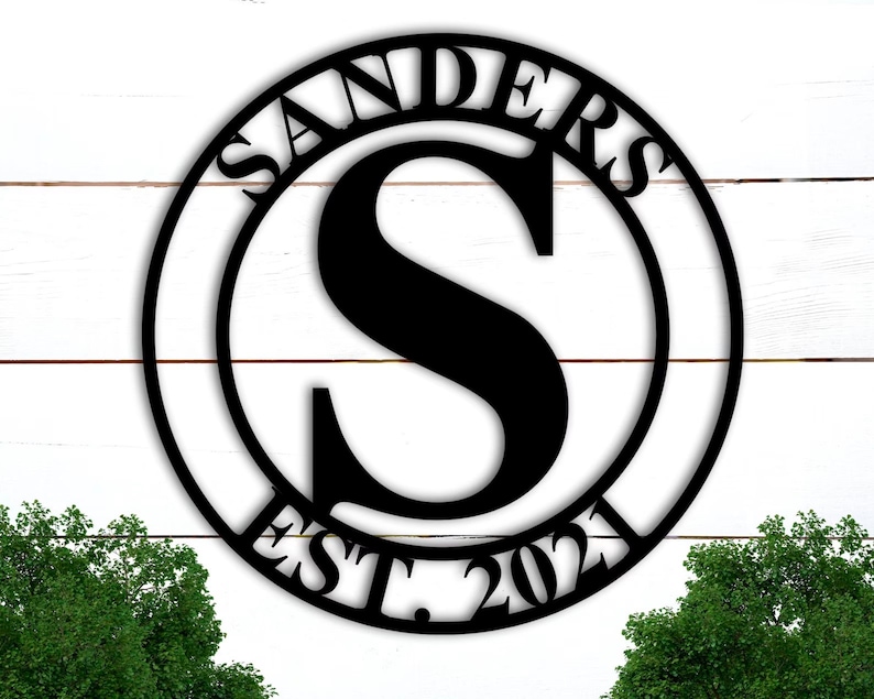 Op de afbeelding: Een zwart metalen rond bord met de achternaam "SANDERS" en het jaar "EST. 2023" rond de buitenkant. De letter "S" bevindt zich in het midden van de cirkel.