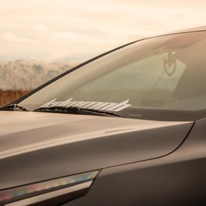 May include: A gray car with a windshield wiper and a sticker on the windshield that says "#hashtag".