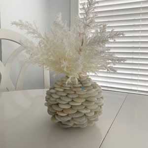 May include: White faux branches in a vase made of stacked white stones. The vase is round and has a smooth, natural finish.