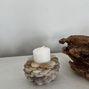 May include: A white candle sits in a candle holder made of small, smooth, gray, brown, and beige stones.