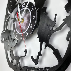 Puede incluir: Reloj de vinilo negro con una silueta de una ni&ntilde;a caminando con un gato. La esfera del reloj tiene un fondo negro con n&uacute;meros y manecillas blancas.