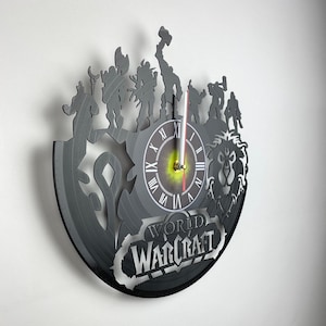 May include: A black vinyl record clock featuring a silhouette of characters from the World of Warcraft video game. The clock face is white with black Roman numerals and a gold center. The clock is surrounded by a black silhouette of characters from the game, including a lion, a warrior, and a mage. The text "World of Warcraft" is printed below the clock face.