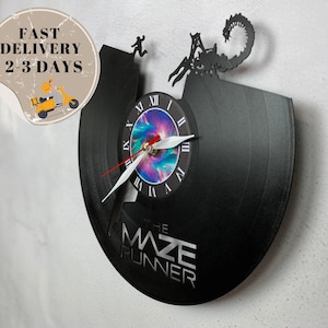 May include: Black vinyl record clock with a galaxy-themed clock face and a silhouette of a creature from the Maze Runner movie. The clock face reads "The Maze Runner".