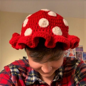 May include: A red crocheted mushroom hat with white polka dots and a ruffled brim.