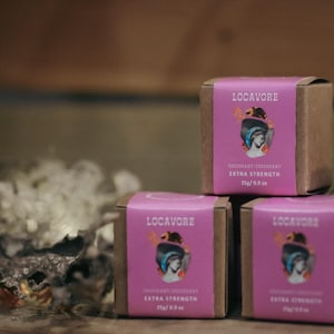 May include: Three small cardboard boxes with pink labels and the text "Locavore" printed on them. The boxes are stacked on top of each other. The labels also say "Fragrant Deodorant" and "Extra Strength" with a 25g/0.8 oz measurement.