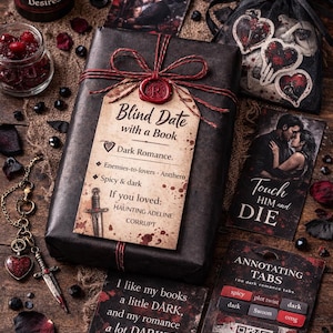 May include: A dark romance gift set featuring a wrapped book with a "Blind Date" tag, a candle, and heart-themed accessories. The book's tag lists romance genre details. The set also includes a small jar of berries and a decorative necklace.