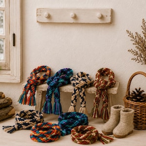 Könnte beinhalten: Eine Sammlung von geflochtenen Garnaccessoires in verschiedenen Farbkombinationen wie Rot, Blau, Grün und Beige. Die Artikel umfassen geknotete Schals mit Quasten, kreisförmige geflochtene Bänder sowie ein Paar Stiefel aus beigem Filz.
