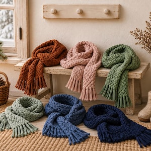 Könnte beinhalten: Eine Kollektion aus sechs grob gestrickten Schals in Rostorange, Altrosa, Salbeigrün, hellem Mintgrün, Mittelblau und Marineblau. Jeder Schal hat ein dickes, strukturiertes Zopfmuster und ist mit langen, geraden Fransen versehen.