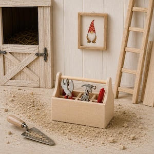 Op de afbeelding: Een miniatuur houten gereedschapskist met een kleine metalen tang, een hamer en een rode schroevendraaier. Een metalen troffel met een houten handvat ligt ernaast. De set bevat een miniatuur schuurdeur, een ingelijste kabouterillustratie en een ladder.