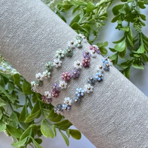 May include: Four beaded bracelets with flower designs in shades of green, purple, blue, and white.