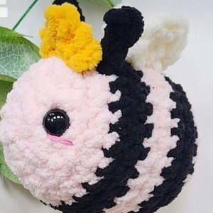 May include: A crocheted bee plush toy with a pink and black striped body, yellow crown, and white wings.