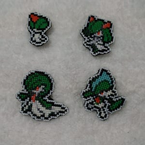May include: Four cross-stitch patches in a pixel art style. The patches feature green, red, white, and blue designs with black outlines. The patches are in the shape of various characters.
